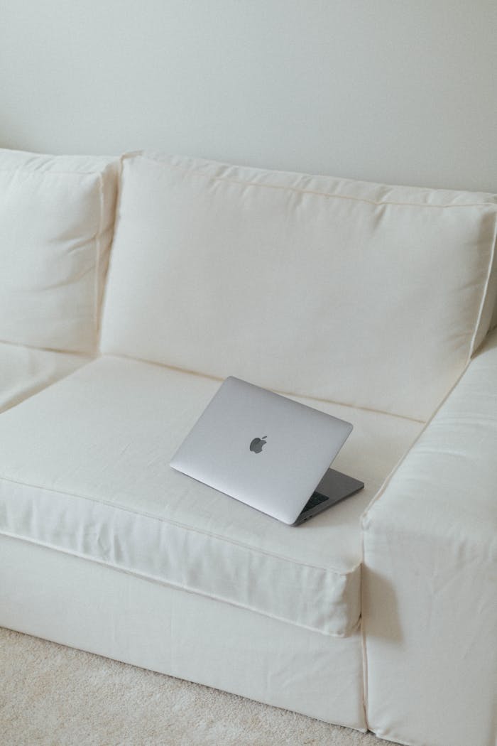 Sleek silver laptop on a clean white sofa in a minimalist setting, ideal for tech or modern lifestyle themes.